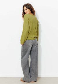 Pull en maille côtelée vert olive avec épaules tombantes, associé à un jean gris à taille haute et large. Des chaussures décontractées complètent le look.