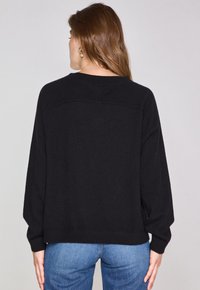 Pull noir à coupe ample, avec des manches larges et un ourlet côtelé, présentant un col rond et un détail de couture subtil au dos.