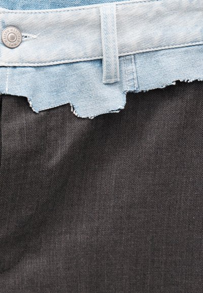 Φαρδύ γαλάζιο τζιν με τραχιά άκρη και ασημένιο κουμπί πάνω σε ενιαίο σκουρόχρωμο γκρι φόντο υφάσματος.