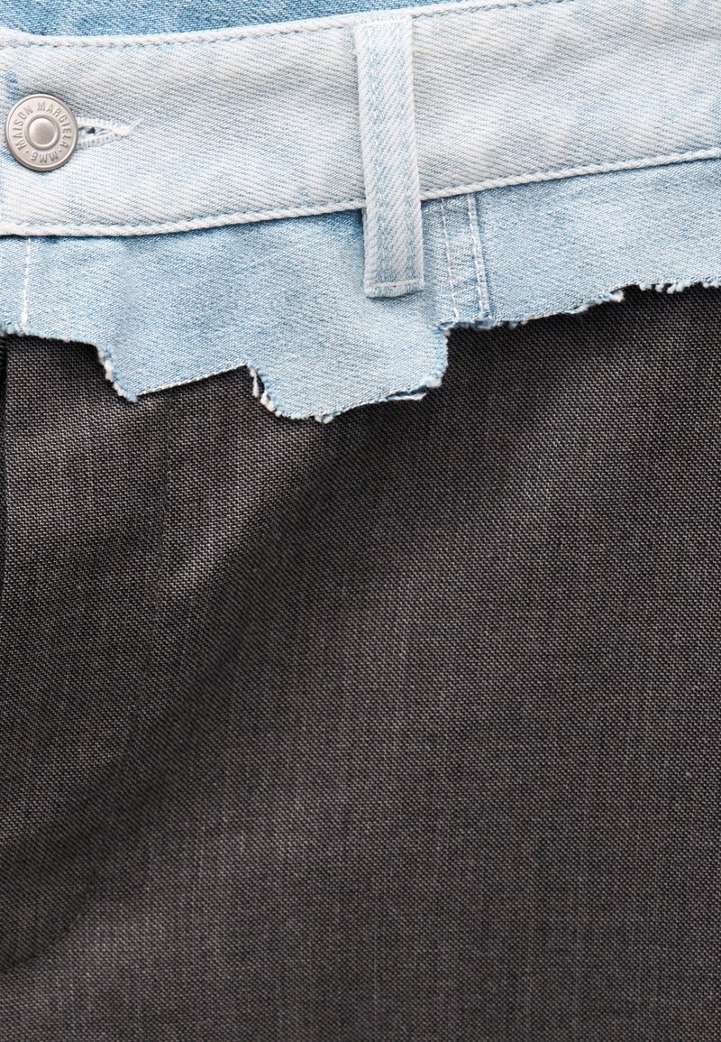 Lichtblauwe denim tailleband met rafelige rand en zilveren knoop boven een effen donkergrijze stoffen achtergrond.