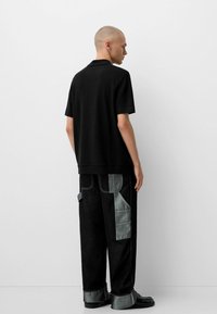 Polo shirt nera a costine abbinata a jeans neri oversize con tocchi di denim chiaro e grandi tasche. Scarpe flat completano l'outfit.