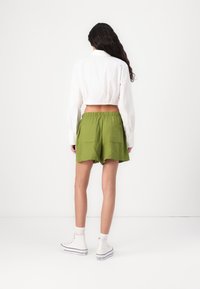 Pantalones cortos de lino verdes con una cinturilla elástica, que cuentan con dos bolsillos traseros, combinados con una camisa blanca corta y zapatillas altas blancas.
