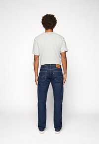 Jeans de mezclilla azul con un diseño de pierna recta, que cuentan con una etiqueta de cuero en la parte posterior, y una camiseta básica gris. Textura uniforme, sin patrones visibles.
