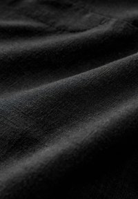 Schwarzer Stoff mit glatter Textur und dezentem Glanz, der durch weiche Falten eine leichte und gut fallende Qualität aufweist.