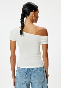 Witte geribbelde off-shoulder top met korte mouwen, aansluitend ontwerp, textiel met textuur, gecombineerd met blauwe hoge taille spijkerbroeken.