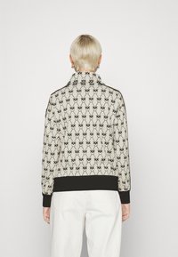 Chaqueta bomber con un patrón en crema y diseño floral negro. Presenta un cuello alto y puños y dobladillo de canalé negro. Textura de tela suave.
