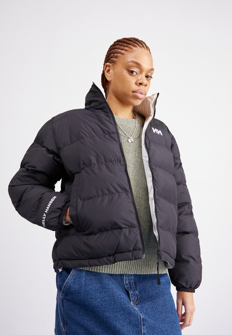 Black puffer jacket with quilted design, featuring a high collar and contrasting gray interior. The brand "Helly Hansen" is printed on the sleeve.