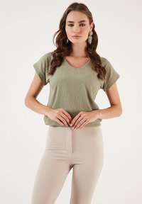 Olive green, short-sleeve top with a v-neck and textured fabric; paired with light beige high-waisted leggings, smooth and fitted.