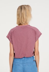 Korte mouwen, mauve t-shirt met een relaxte pasvorm en ronde halslijn. Zachte stoftextuur. Gecombineerd met lichtblauwe broek met elastische tailleband.