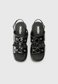Black synthetic sandals feature two buckled straps, smooth texture, contrasting white stitching, and a cushioned footbed with logo.