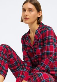 Rødrutete pysjamassett med blå og grønn aksent; knappetopp med krage og lange ermer, kombinert med matchende løstsittende bukser.