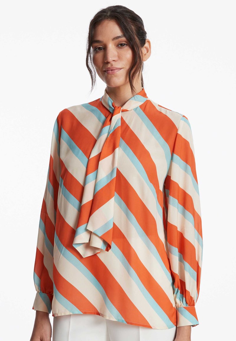 Seidenbluse mit langen Ärmeln, die diagonale orange, hellblaue und cremefarbene Streifen aufweist, sowie ein Schleifenkragen-Detail.