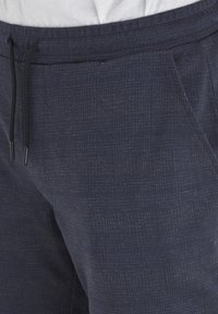 Tmavo modré tepláky s jemným textúrovaným vzorom, vybavené elastickým pásom s šnúrkou a bočnými vreckami.