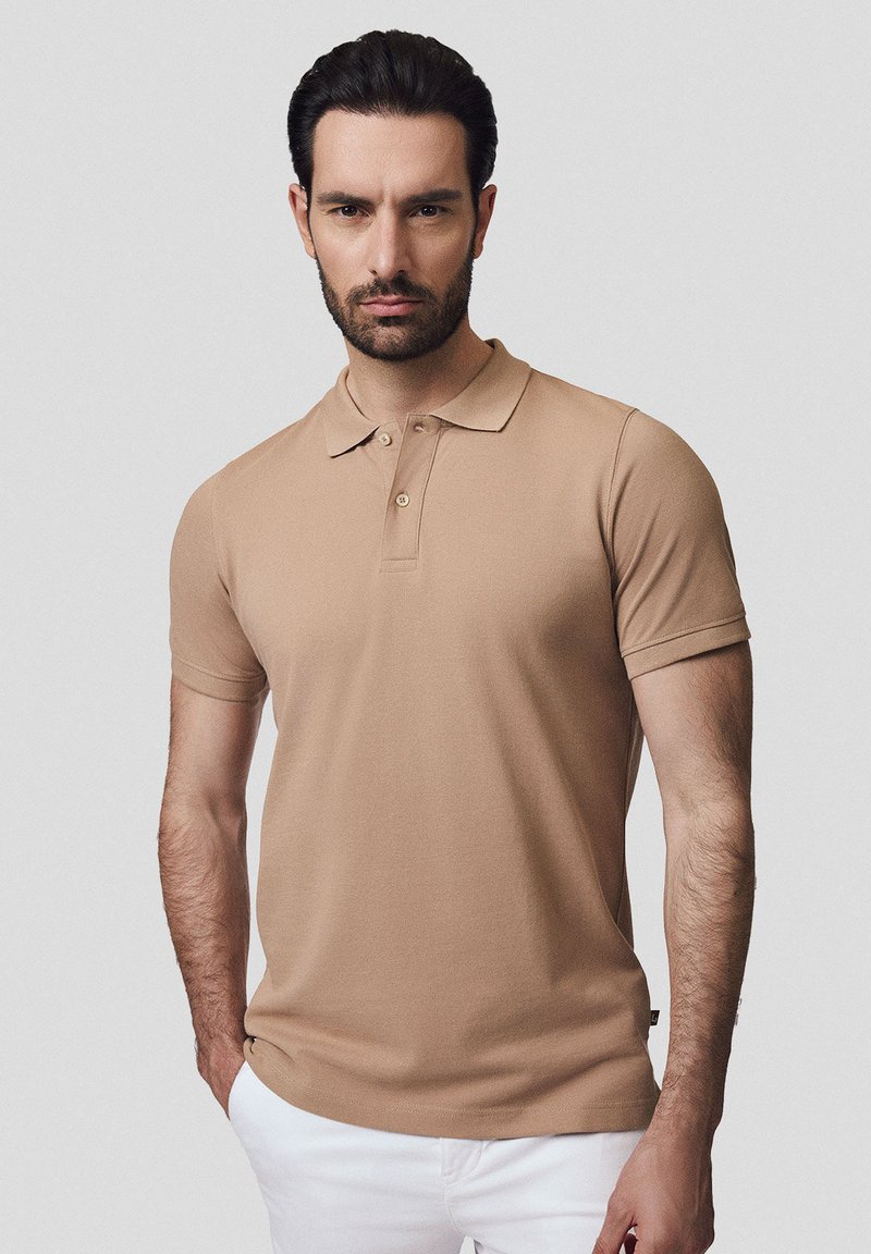 Beżowa koszulka polo z klasycznym kołnierzykiem, krótkimi rękawami i dopasowanym krojem. Wykonana z gładkiego materiału z dwoma guzikami przy dekolcie.