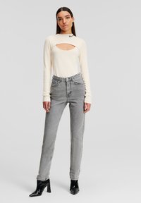 Krämfärgad långärmad topp med ett utskärning, kombinerad med h�öga grå jeans. Svarta klackboots fulländar outfiten. Släta texturer genomgående.