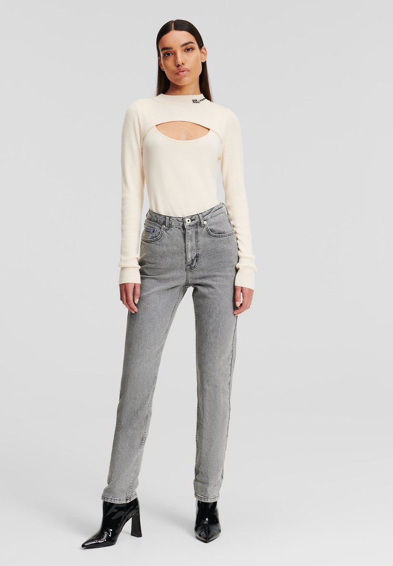 Krämfärgad långärmad topp med ett utskärning, kombinerad med höga grå jeans. Svarta klackboots fulländar outfiten. Släta texturer genomgående.