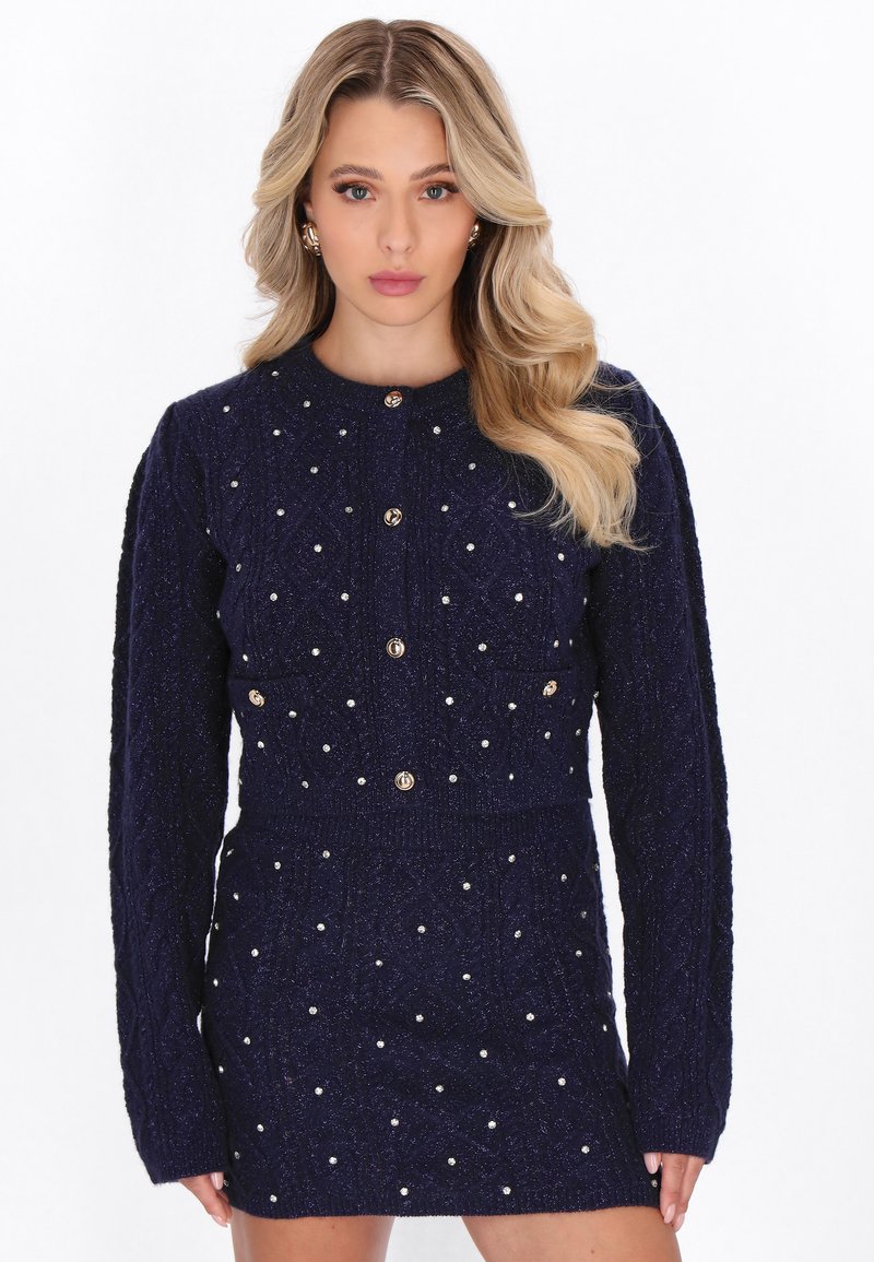 Meriharmaa neulemekko pitkilla hihoilla, pyöreällä kaula-aukolla, jossa on helmimäisiä koristuksia ja metalliset nappikiinnitykset edessä.