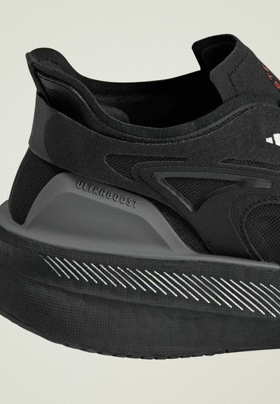 Scarpa sportiva nera con una parte superiore in rete testurizzata, suola ammortizzata e un distintivo'etichetta 'ULTRABOOST' sulla parte laterale, caratterizzata da linee di design eleganti.