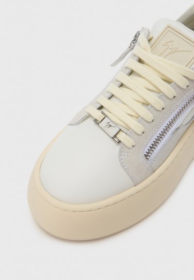 Close-up van een crème sneaker met dikke veters, een zilveren rits aan de zijkant, suède details en een beige rubberen zool.