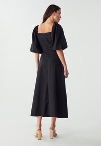 Black midi dress with puff sleeves, square neckline, and a fitted bodice featuring horizontal pleats. Smooth texture, side zipper closure.