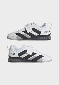 Bijele sportske tenisice s crnim akcentima, teksturirano mrežasto gornjište, podesivi remen i uzorčena potplata. Sadrži natpis "Snaga u brojevima".