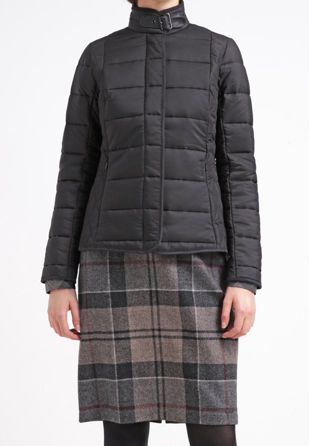 Femme porte une veste matelassée noire avec un col à boucle et une jupe grise à carreaux longueur genou avec des collants noirs.