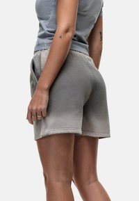 Pantaloni corti in cotone grigio con un design a gradiente, dotati di tasche laterali e orli cuciti, mostrati da un'angolazione laterale.