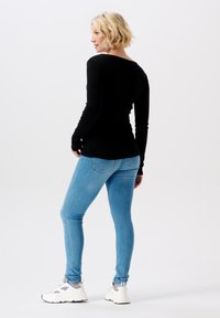 Zwarte lange mouwen top met een nauwsluitend design, gecombineerd met lichtblauwe skinny jeans en witte sportschoenen, met een ronde halslijn en een gladde textuur.