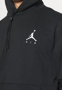Felpa nera con cappuccio realizzata in tessuto morbido; presenta una chiusura con cordino e un logo Jumpman bianco con il testo "AIR" ricamato sotto.
