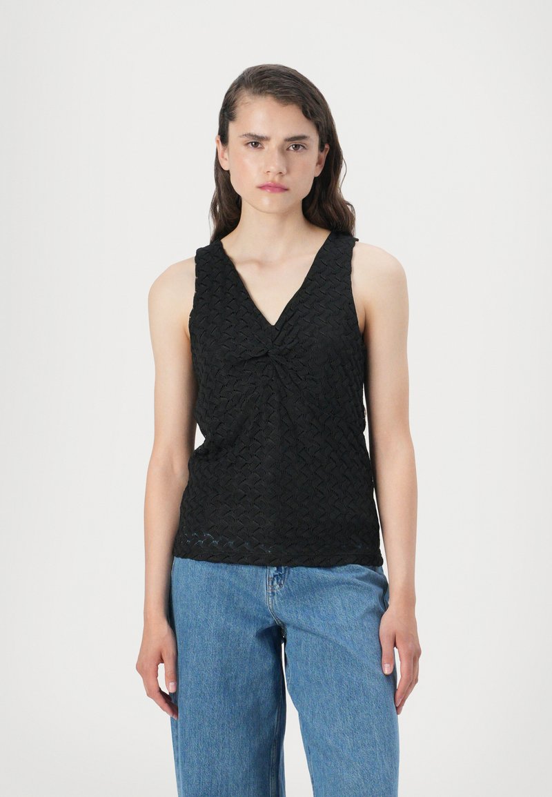 Top preto sem mangas com decote em V e detalhe frontal torcido, apresentando um padrão texturizado, combinado com jeans de perna larga azul claro.