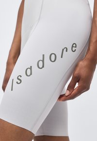 Κοντινή λήψη ενός ατόμου που φοράει ανοιχτό γκρι ποδηλατικά σορτς με την επιγραφή "Isadore" τυπωμένη κάθετα με σκούρα γράμματα στον μηρό.
