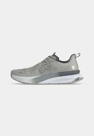 Baskets athlétiques grises et blanches avec lacets, logo EA7 Emporio Armani sur le côté et languette au talon sur fond uni.