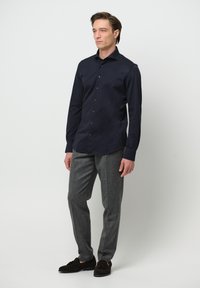 Marinefarbendes Hemd mit Knöpfen, taillierte Passform, lange Ärmel. Graue, texturierte Hose, gerade geschnitten. Dunkle Schuhe mit Schleifenakzent. Minimalistisches Design.