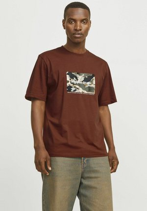 Brown cotton t-shirt with a camouflage print patch featuring "Originals Studio" text. Relaxed fit, short sleeves, round neckline.