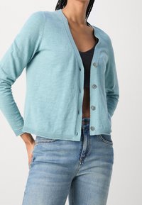 Cardigan bleu clair en tricot doux avec un col en V et cinq boutons à l'avant. Il possède des manches longues et des poignets et ourlet côtelés.