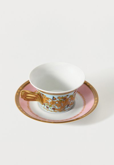 Πορσελάνινο φλιτζάνι τσαγιού με χρυσή λαβή και περίπλοκο πορτοκαλί σχέδιο με λουλούδια και πεταλούδες, τοποθετημένο σε ροζ και λευκό πιατάκι με χρυσό περίγραμμα.