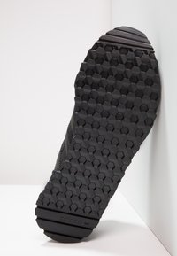 Musta lenkkarin pohja, jossa on kuusikulmainen kuvio, teksturoitua kumia ja Adidas-brändäys. Tasainen muotoilu, jossa kestävä pito.