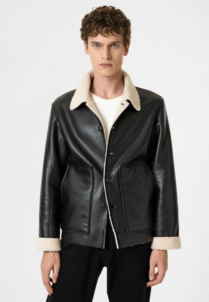 Veste en cuir noire avec un col et des poignets en fausse laine beige, dotée de deux poches avant et de boutons noirs sur la patte de boutonnage.