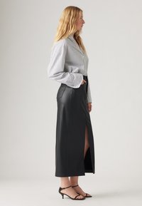 Jupe maxi en cuir noir avec une fente à l'avant, associée à une chemise à rayures à boutons. Présente une coupe ajustée et des manches longues. Talons aiguilles noirs à lanières.