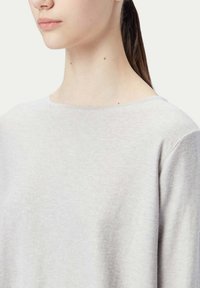 Ljusgrå tröja i mjukt material med båthals och lös passform. Synlig sömnad vid axlarna och halsringningens kanter.