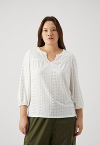 B balta blūze ar trīs ceturtdaļu piedurknēm, ar acu izšuvumu, apaļu kakla izgriezumu un savilkuma detaļu plecos.