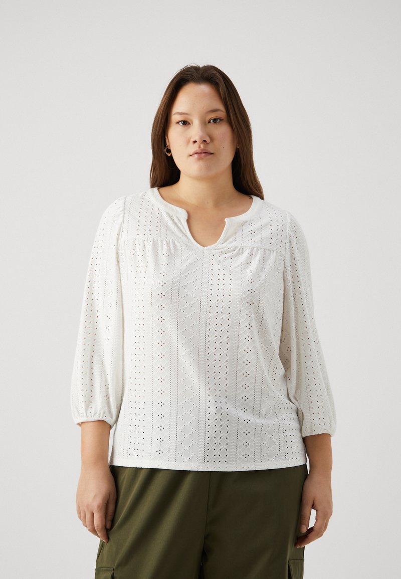 B balta blūze ar trīs ceturtdaļu piedurknēm, ar acu izšuvumu, apaļu kakla izgriezumu un savilkuma detaļu plecos.