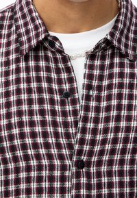 Camicia a quadri rossonera con dettagli bianchi, caratterizzata da un design a bottoni e un bottone nero sul colletto. Tessuto di cotone, con motivo testurizzato.