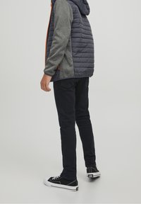 Kurtka ocieplana z szarymi rękawami, ciemnoniebieskim korpusem, pomarańczowym zamkiem, czarnymi spodniami i czarnymi trampkami z białymi podeszwami, widziana z tyłu.