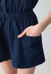 Combinaison en lin bleu marine avec une taille élastique, coupe ample et une poche latérale, le tout avec une finition douce et texturée.