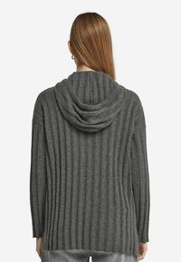 Szary sweter z prążkowanej tkaniny, z kapturem, długimi rękawami i bocznymi rozcięciami u dołu. Materiał wydaje się teksturowany i miękki, odpowiedni do codziennego użytku.