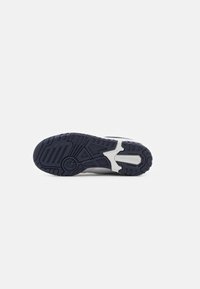 Semelle extérieure en caoutchouc d’une chaussure New Balance montrant une bande de roulement noire avec des motifs et le nom de la marque dans la partie blanche de la semelle intermédiaire.