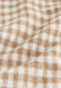 Hnědá a bílá kostkovaná látka s tkanou texturou a mřížkovým vzorem, zobrazující měkká, přírodní vlákna.