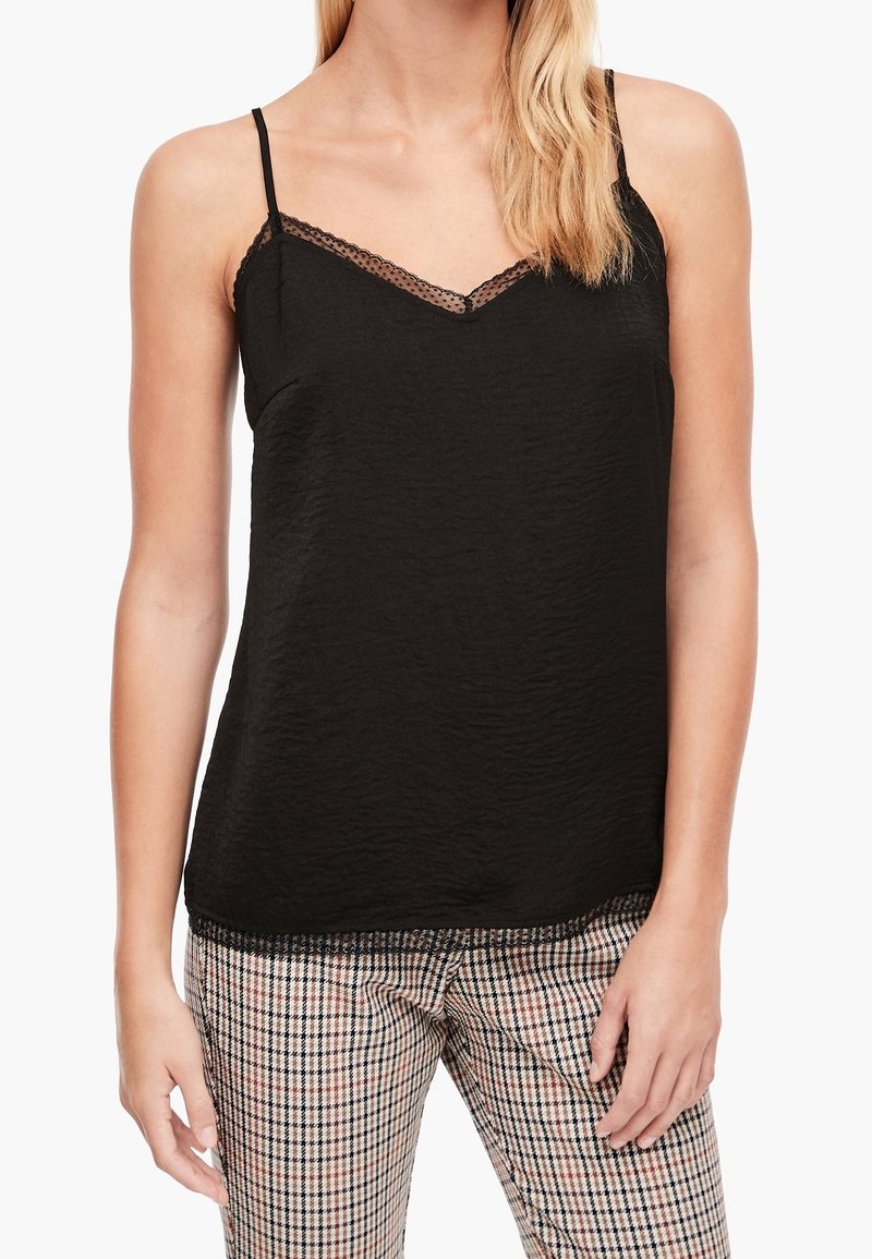 Svart ärmlös linne med v-ringning, med spetskant längs halsringningen och fållen. Bärs med mönstrade rutiga byxor.