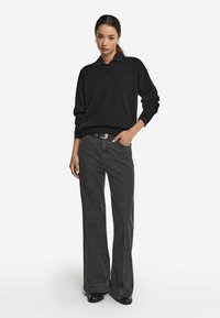 Czarny sweter z dzianiny w serek, zestawiony z czarnymi spodniami typu wide-leg na wysokim stanie. Srebrna klamra paska, gładka tekstura, prosty design.